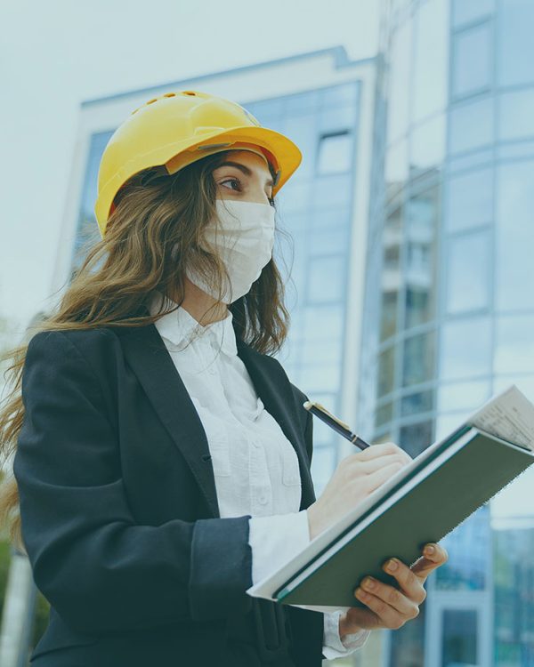 Female architect with construction site on the background Girl builder with folder. Woman standing against the background of the city. Coronavirus theme.